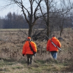 Two hunters wearing blaze orange walking away from camera.